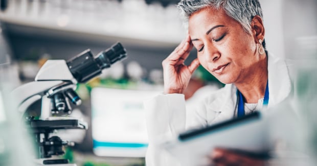  A concerned scientist in a lab coat reviews data on a tablet beside a microscope, reflecting the pressure of responding to an FDA warning.