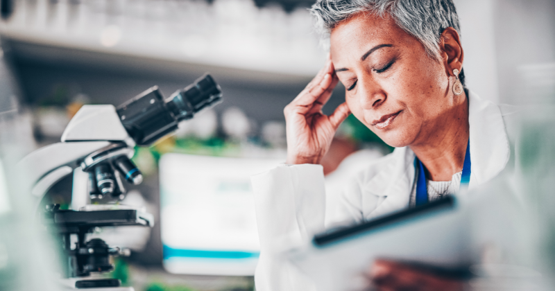 A concerned scientist in a lab coat reviews data on a tablet beside a microscope, reflecting the pressure of responding to an FDA warning.
