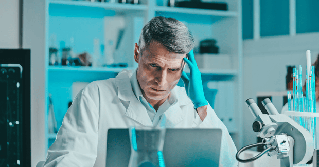 A pharma lab technician looks at his laptop with a worried expression.