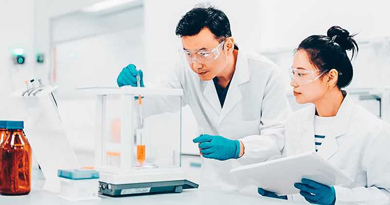 Two scientists working with a weighing scale and ERP solution in a pharma manufacturing facility
