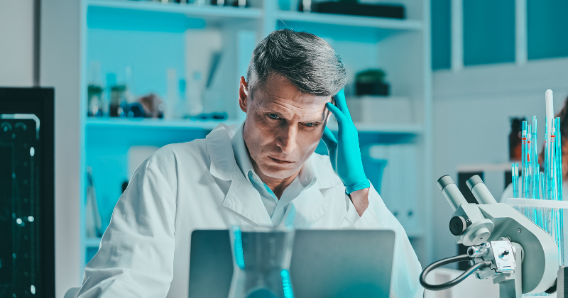 A pharma lab technician looks at his laptop with a worried expression.